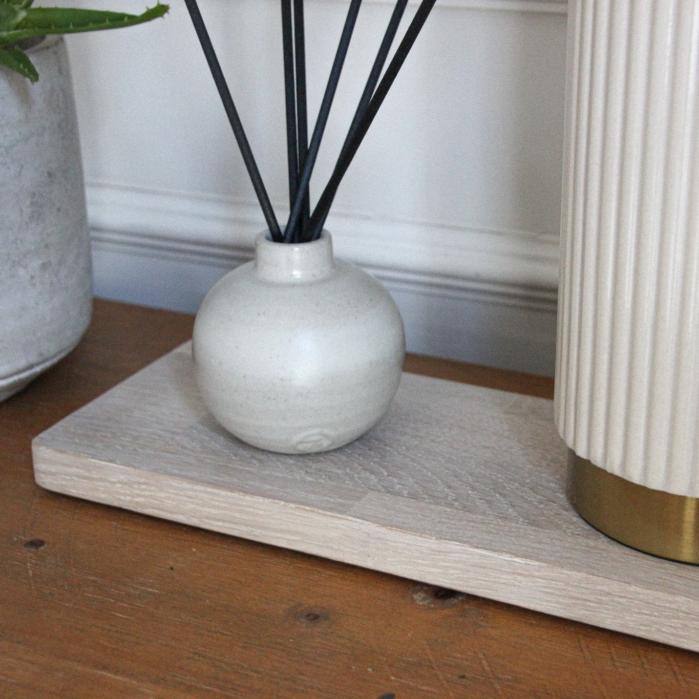 Decorative items including a white diffuser, black reeds, and a plant on a rectangular limed oak wooden mat