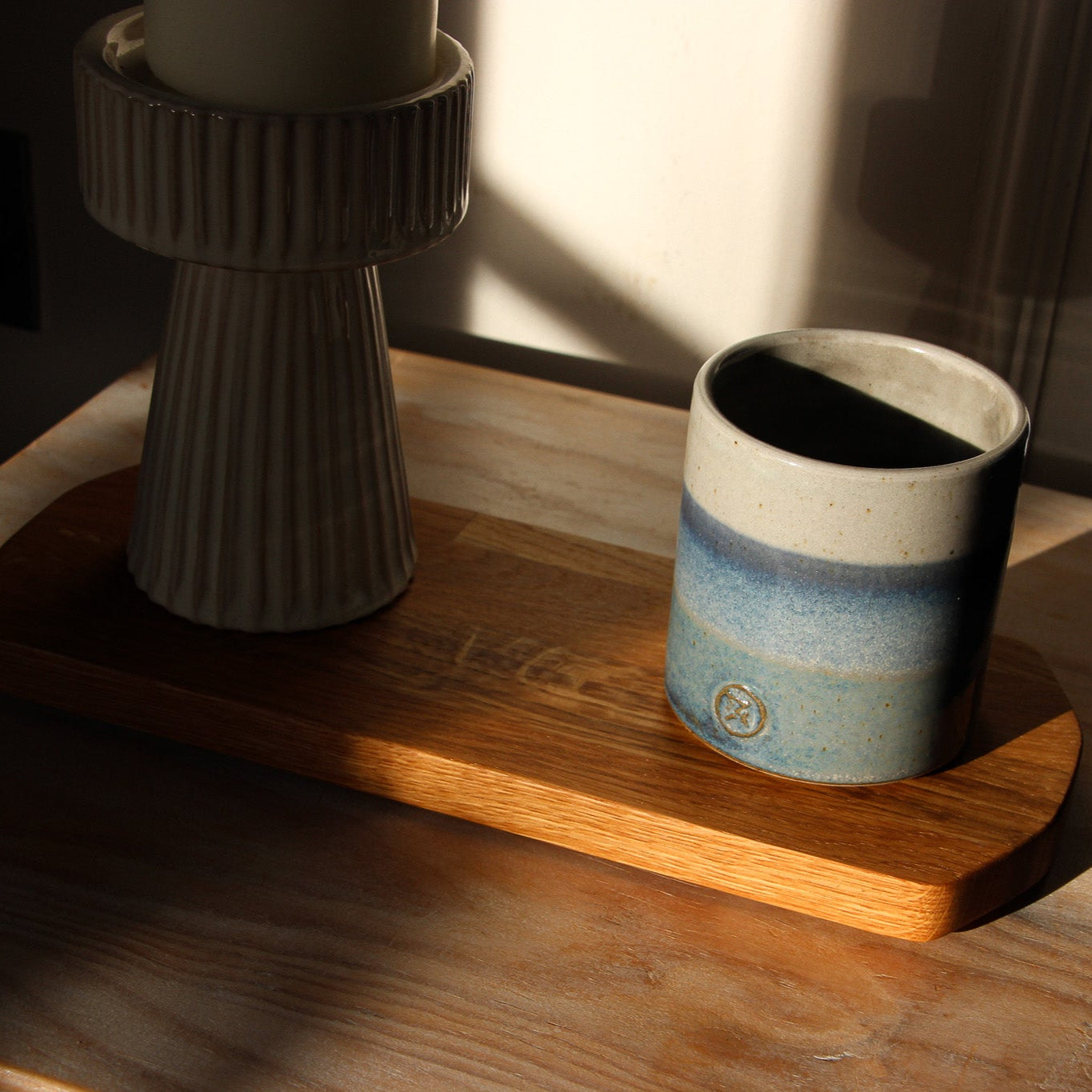 Ceramic cup with blue gradient on a oblong wooden tray in oiled oak with a textured candle holder.
