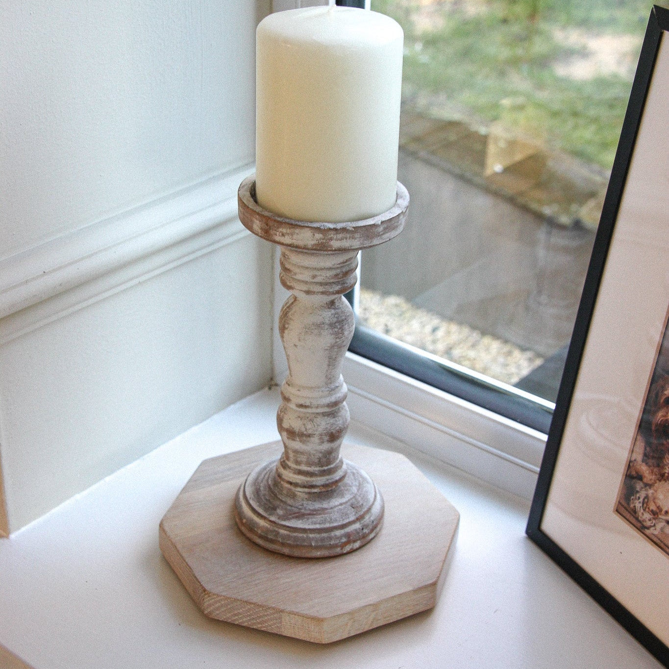Decorative wooden candle holder with a white candle on a windowsill. The holder is placed on a 50 pence piece shaped styling mat.