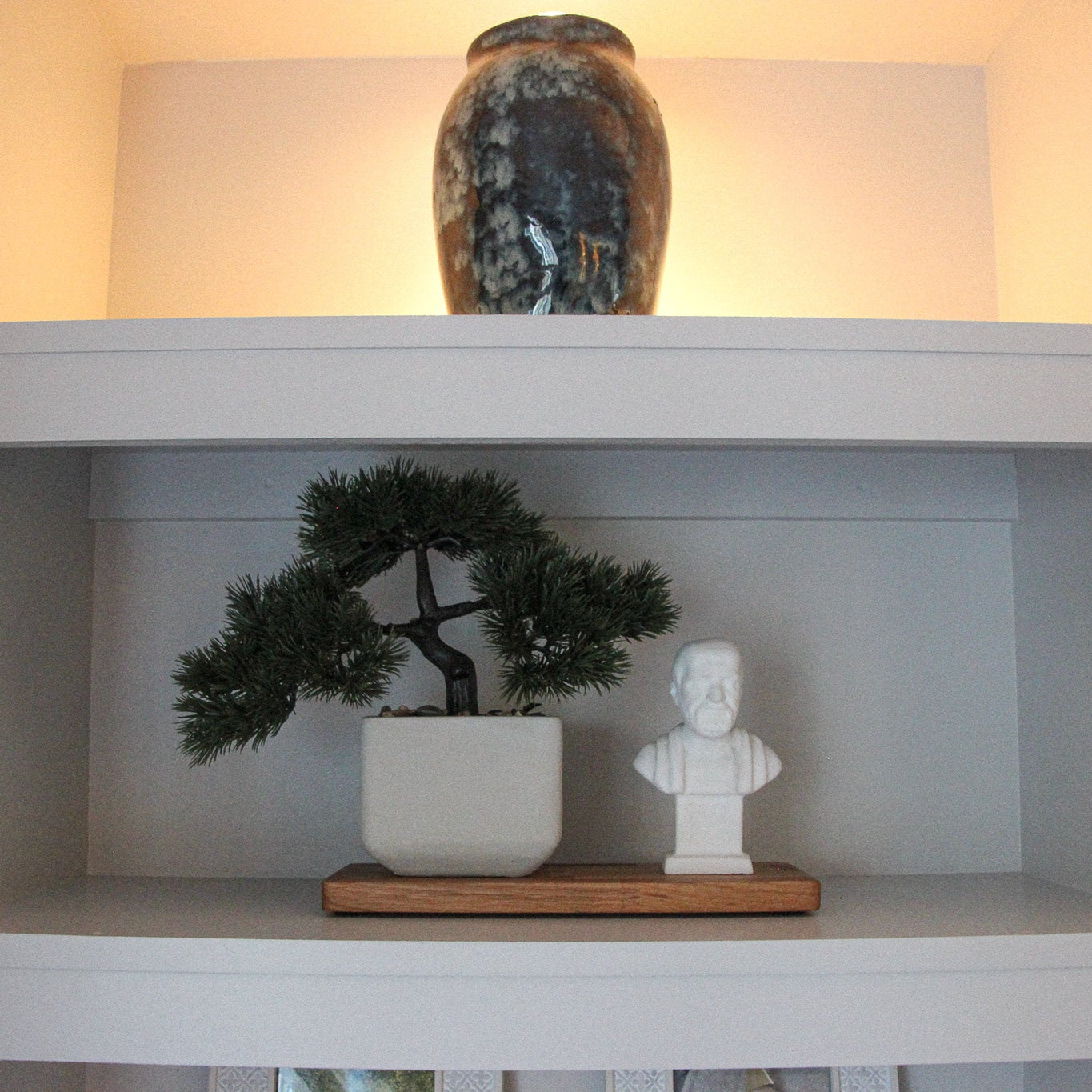 Decorative media wall with a vase, bonsai tree and statue placed on a rectangle oiled oak display tray.