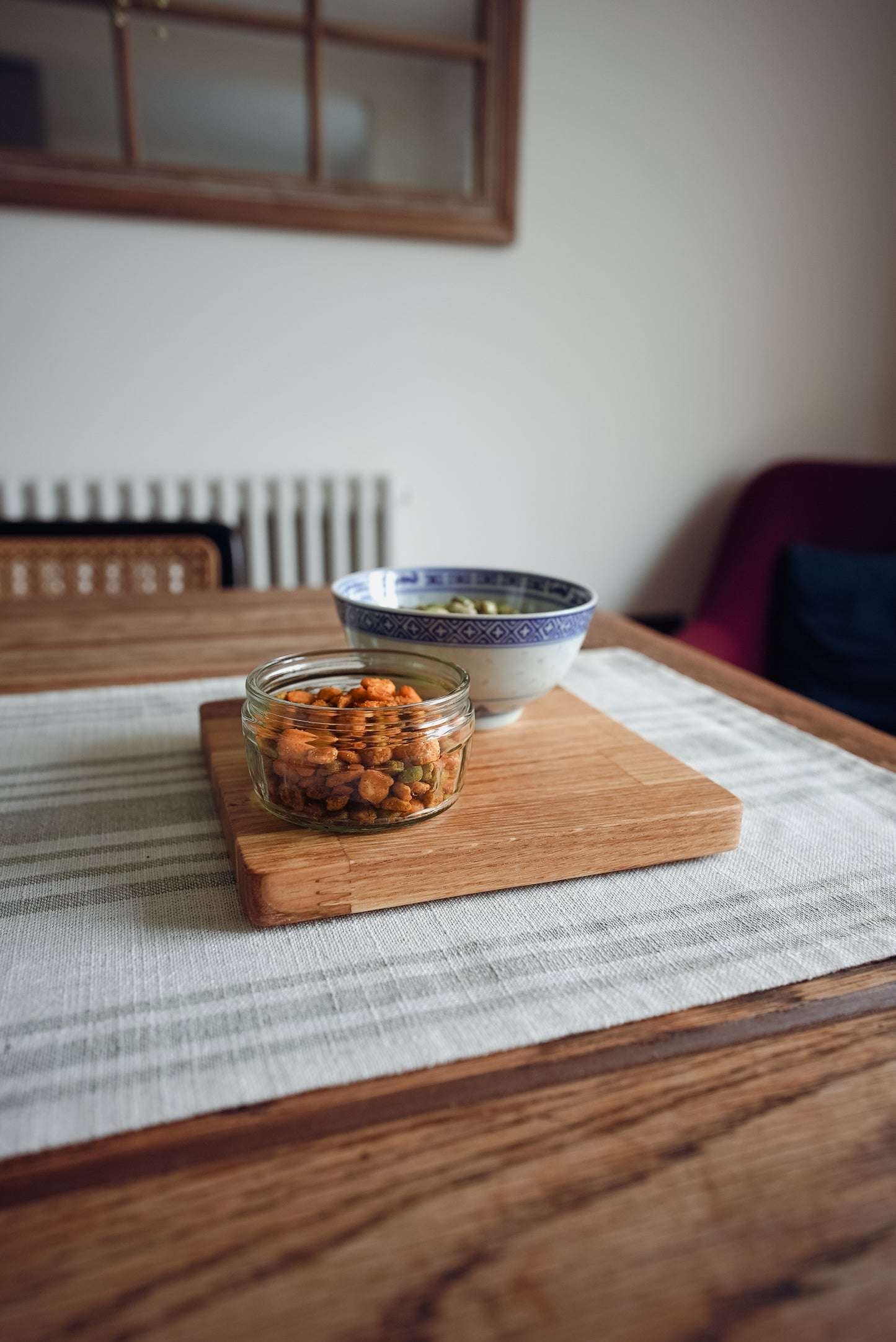 Jar of snacks on a wooden cutting board with a bowl in the background on a table. The image clearly shows the joins of the engineered oak board which forks into each other