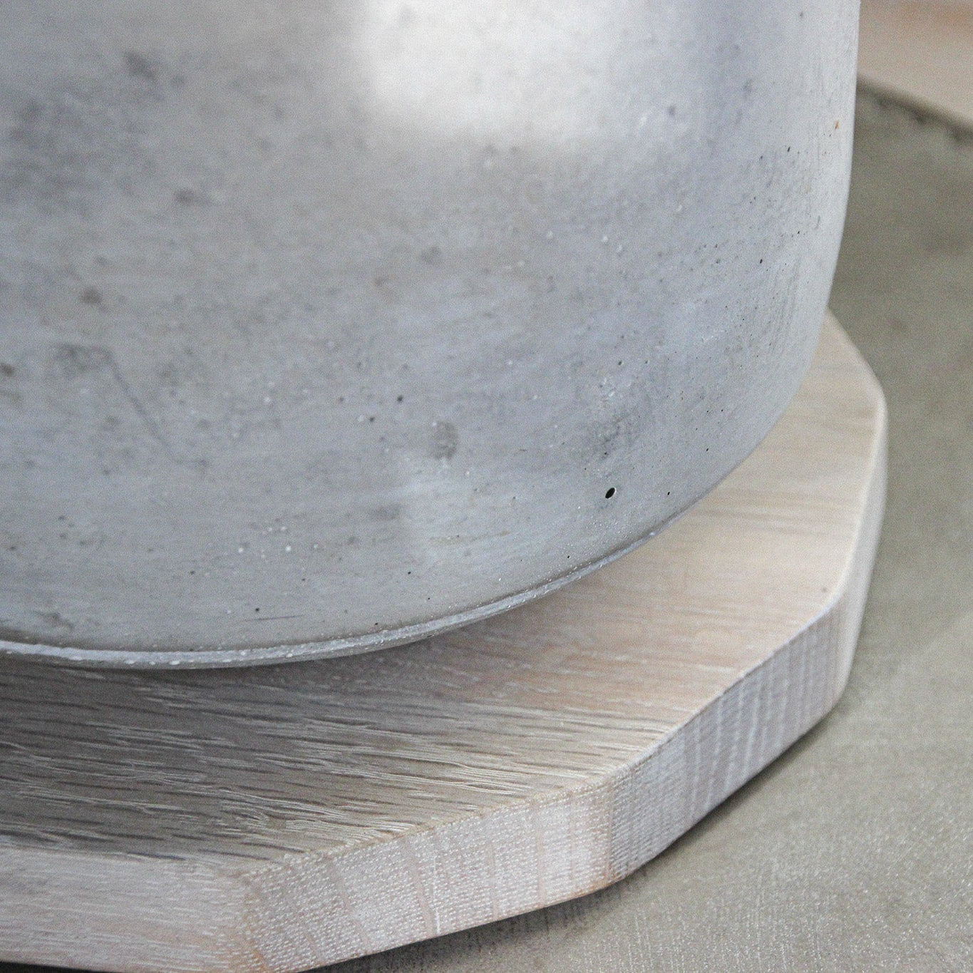 Close-up of a concrete plant pot on top of a light oak display mat shaped like a 50 pence piece