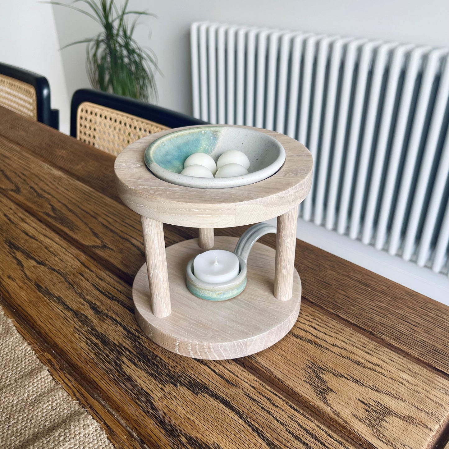 Round shaped wooden wax melt burner in clean limed oak shade with sage glazed pottery tealight spoon and wax melt dish on a windowsill