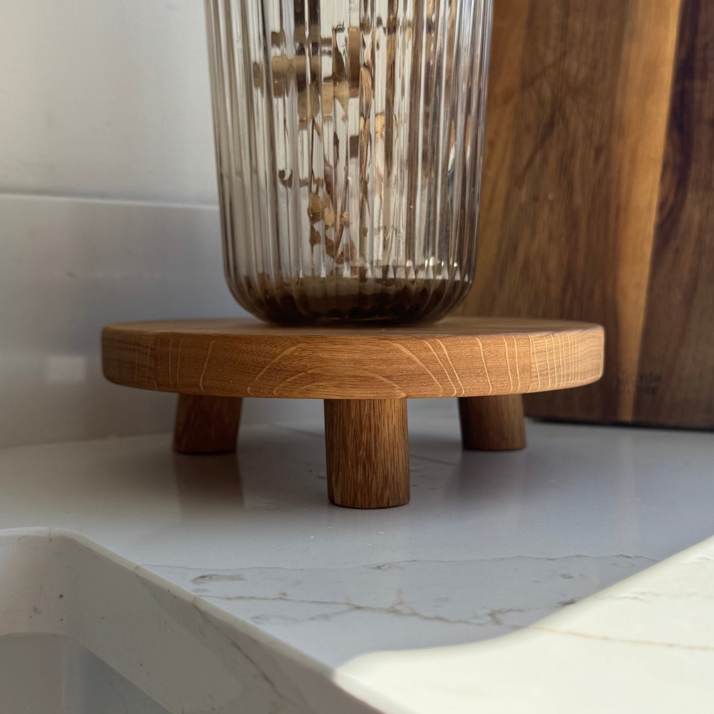 Wooden stand with 3 legs showing the natural grain in an oiled oak stand with a glass vase on a marble surface