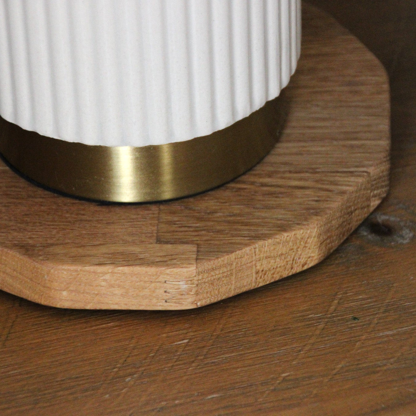 Close-up of a white cylindrical object with a gold base on an oiled oak wooden display mat that has jiggered edges like a 50 pence piece