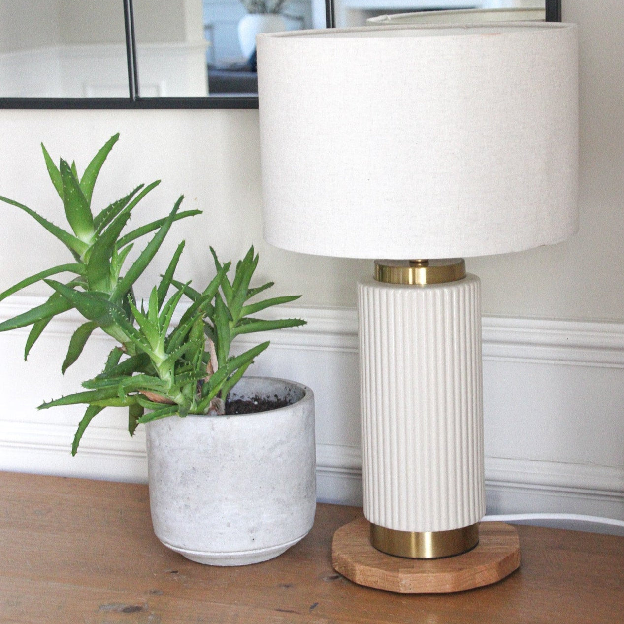 White table lamp with gold base next to a potted plant on a wooden display mat with 50 pence piece side edges in an oiled oak shade.