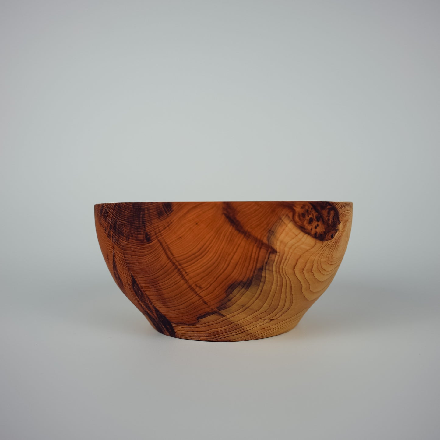 A handcrafted wooden bowl with a rich, swirling grain pattern in warm brown and golden tones, photographed against a neutral light gray background.