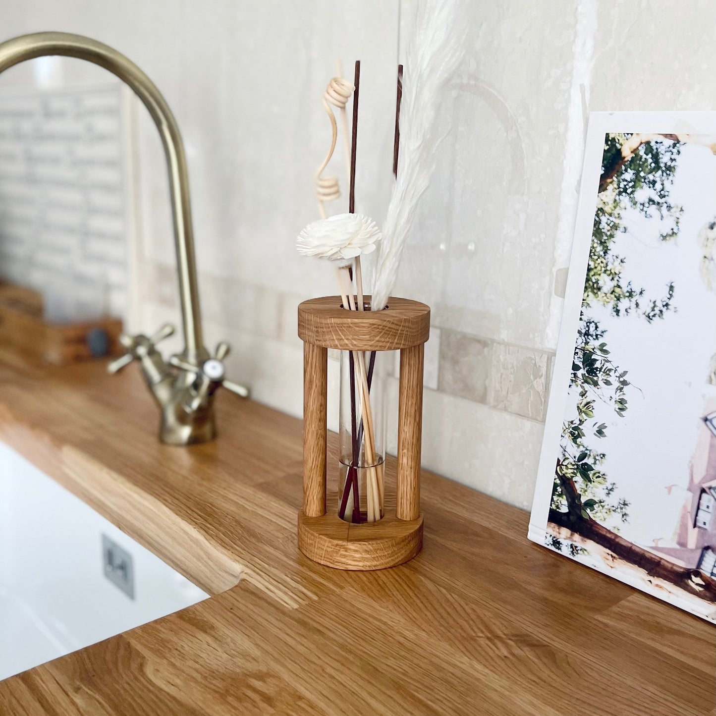 Warm oak coloured frame with a glass vessel inside, filled with diffuser oil with floral reeds popping out of the top