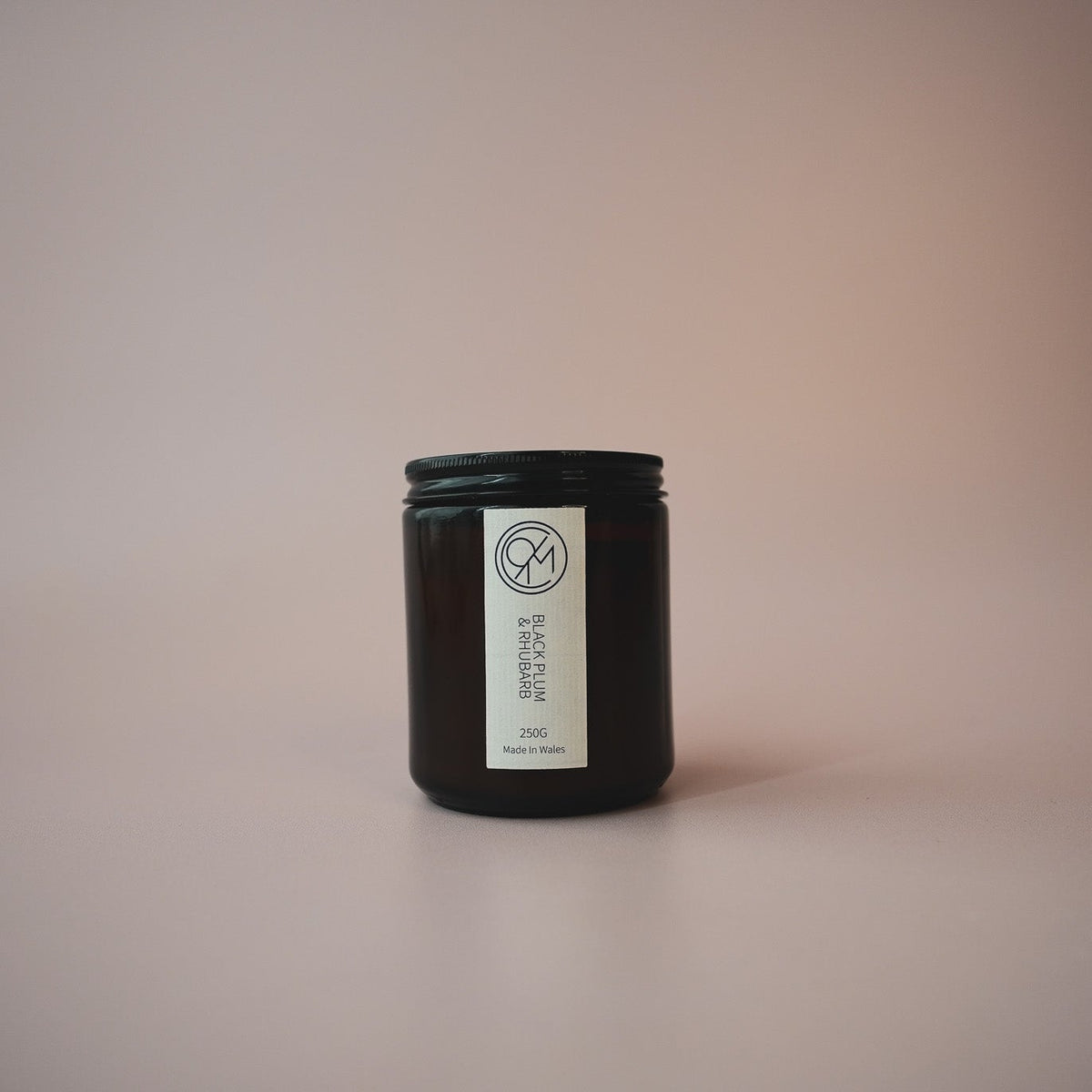 A small amber jar candle with a white label reading 'black plum & rhubarb' on a soft beige background.