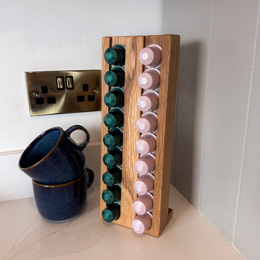 Small wooden coffee pod stand with 18 green and pink coffee pods stacked, blue mugs next to it.