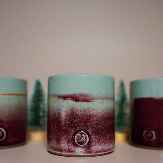 3 pottery candles shown with 2 mini christmas trees in between, each pot has it's own unique dark red glaze