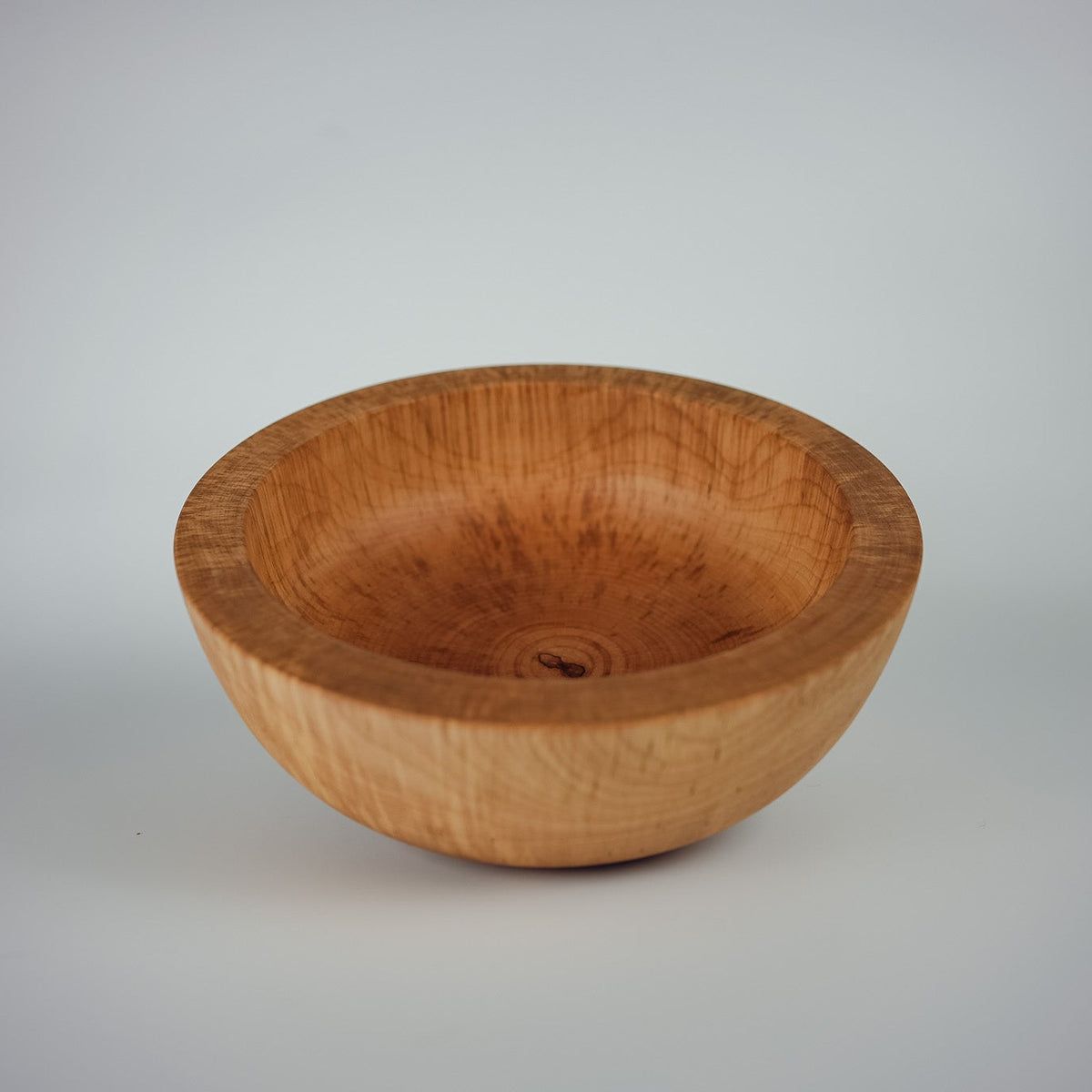 A thick and chunky handcrafted wooden bowl with a visible natural wood grain pattern, photographed on a neutral light white background.