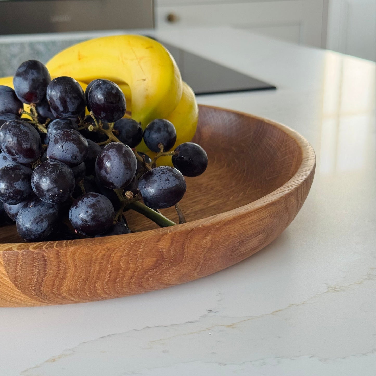 Close up of hand-thrown fruit bowl made from oak with grapes and a banana on a kitchen counter
