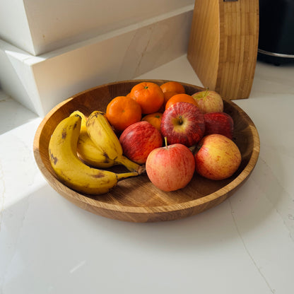 Large shallow wooden bowl with bananas, apples, and oranges on a white surface