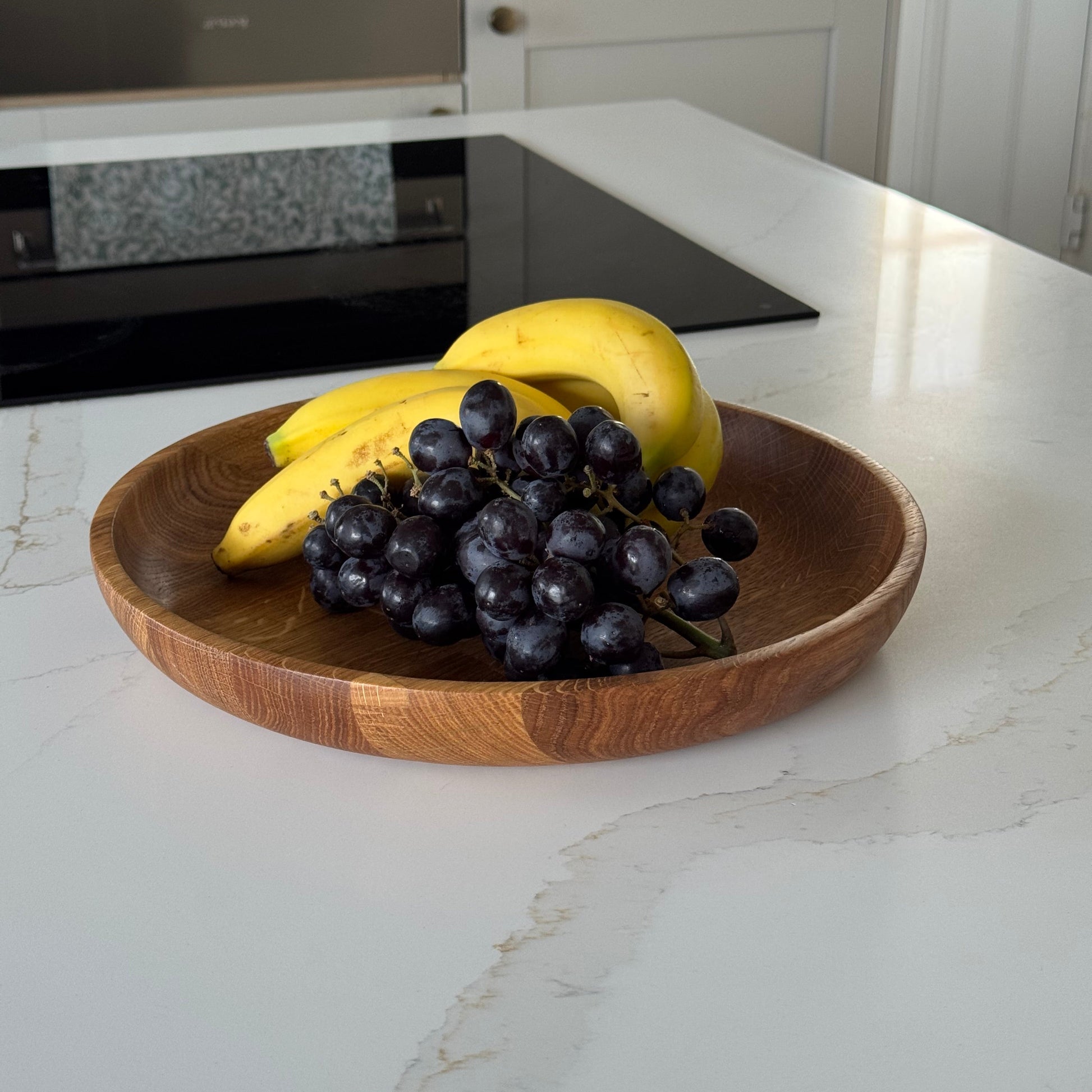 Large oak bowl with grapes and bananas on a kitchen counter