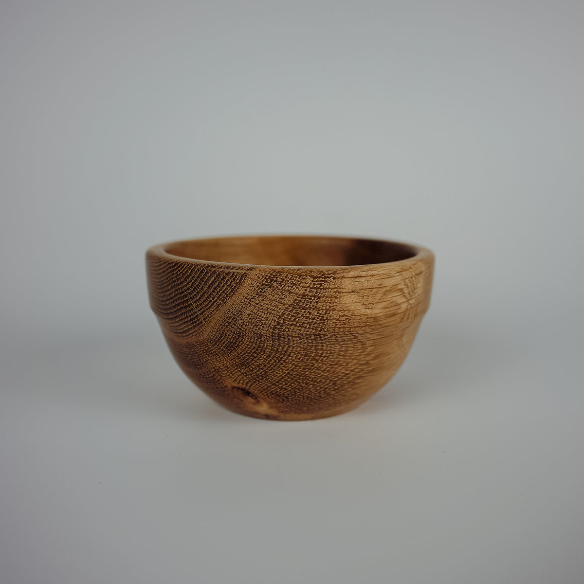 A small handcrafted wooden bowl with a textured, carved grain pattern, shown against a neutral light gray background.