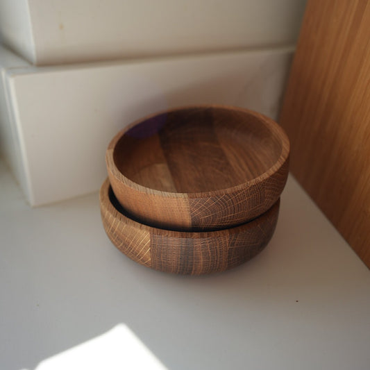 Two hand-turned oak wooden bowls stacked on top of each other, displaying the natural grain and warm tones of the wood.