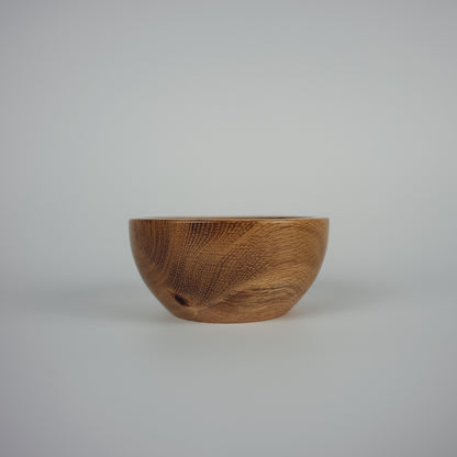 A small handcrafted wooden bowl with a rich brown grain pattern, photographed against a seamless light gray studio background.