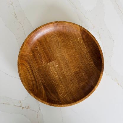 Wooden bowl on a light marble surface, the image is taken from a birds eye view to show the oiled oak finish which shows the natural grain of the wood in an orangey tone.