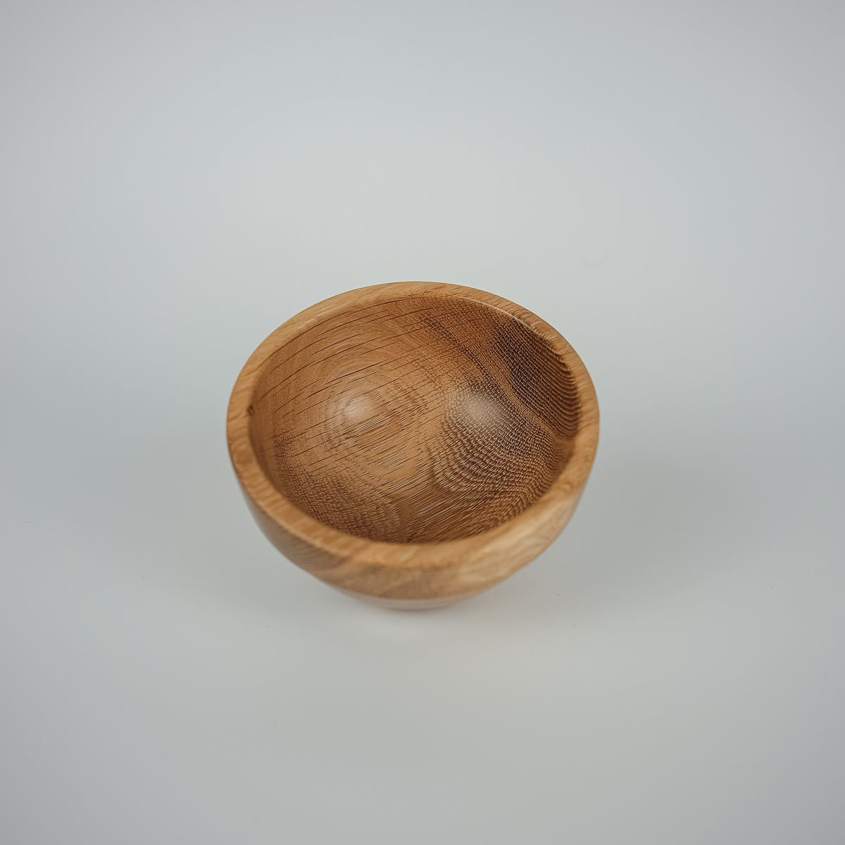 A small handcrafted wooden bowl with a smooth, rounded interior and visible natural wood grain, photographed on a seamless light gray background.