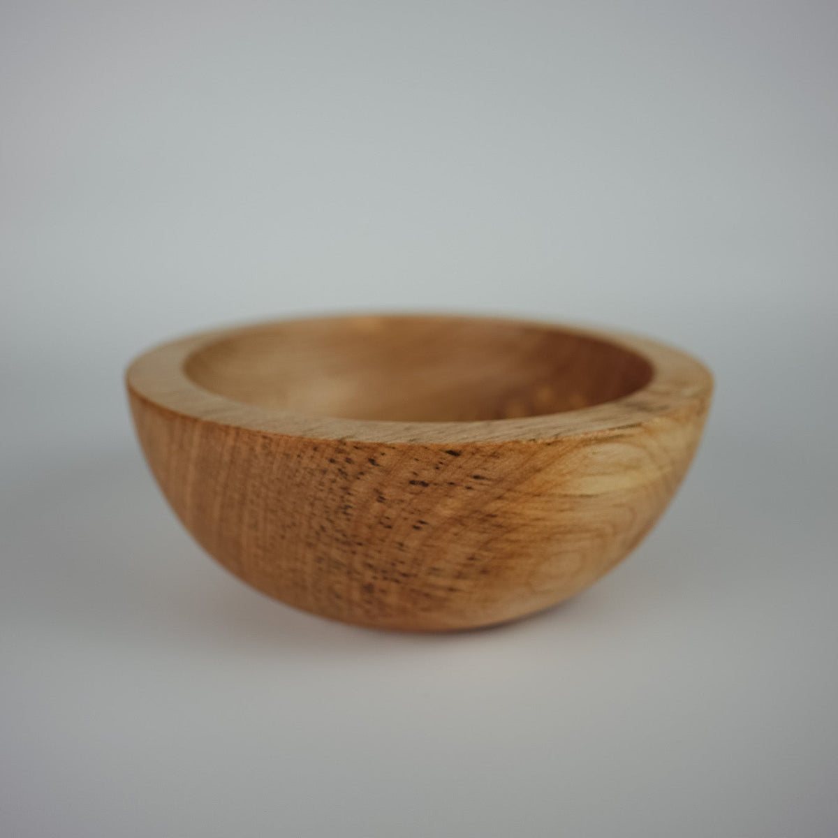 A chunky handcrafted wooden bowl with a natural light brown finish, shown on a neutral light gray background.