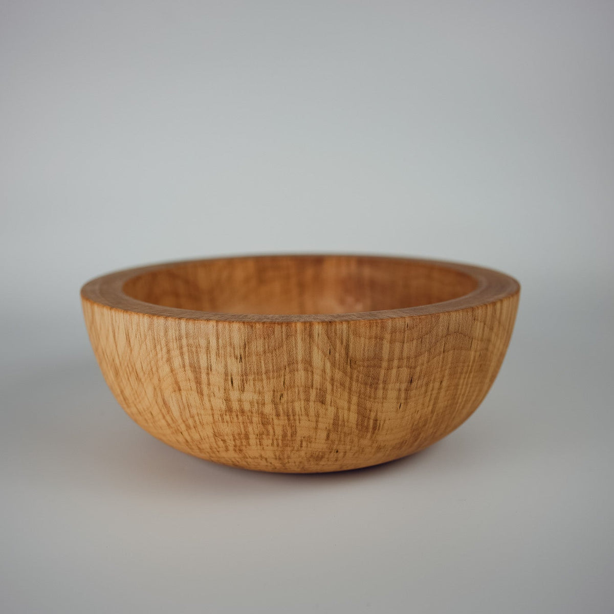 A large handcrafted wooden bowl with a visible natural grain pattern, photographed on a neutral light whitebackground.