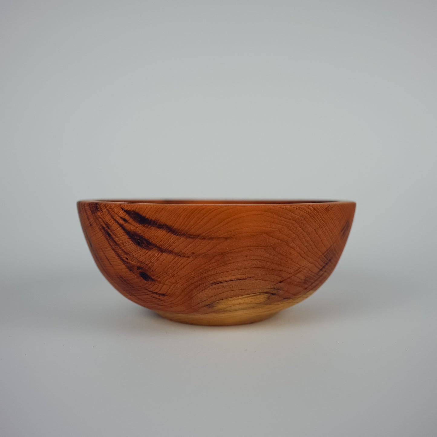 A handcrafted wooden bowl with a rich warm brown finish and dark grain patterns, photographed against a neutral light gray background.