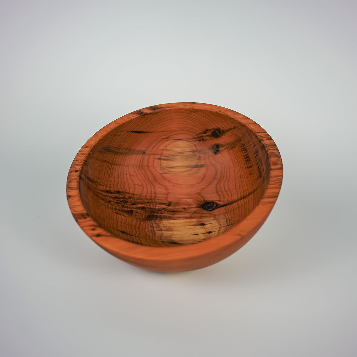 A handcrafted wooden bowl with a warm reddish-brown finish and prominent natural wood grain patterns, photographed on a neutral light gray background.