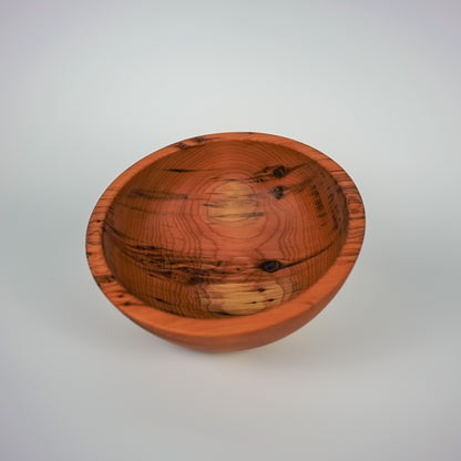 A handcrafted wooden bowl with a warm reddish-brown finish and prominent natural wood grain patterns, photographed on a neutral light gray background.