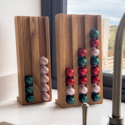 The large and small coffee pod holders on white worktop next to a grey window frame, the coffee pod stand are holding coffee capsules on colours red, pink and green and the shape of the coffee pod organiser is tall and rectangular