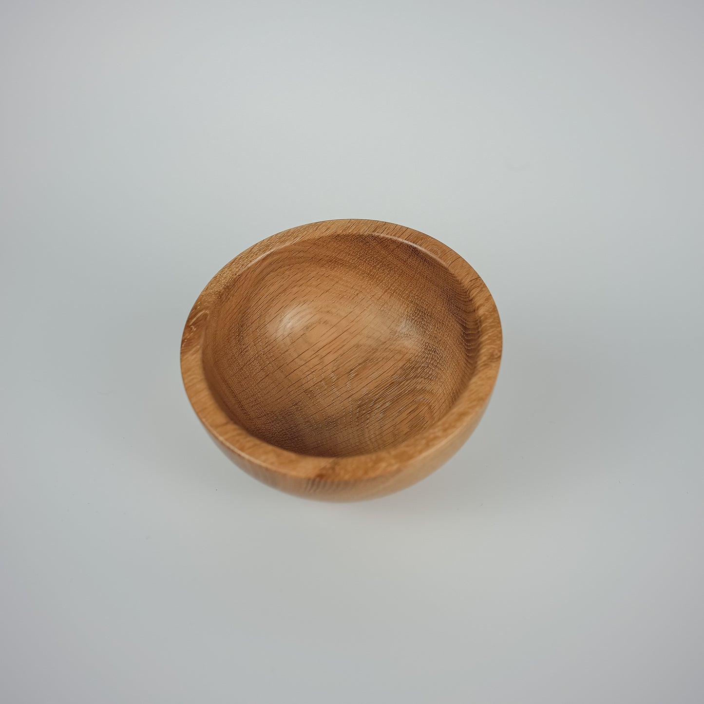 A small, round wooden bowl with a smooth, polished finish and visible wood grain, set against a plain light gray background.