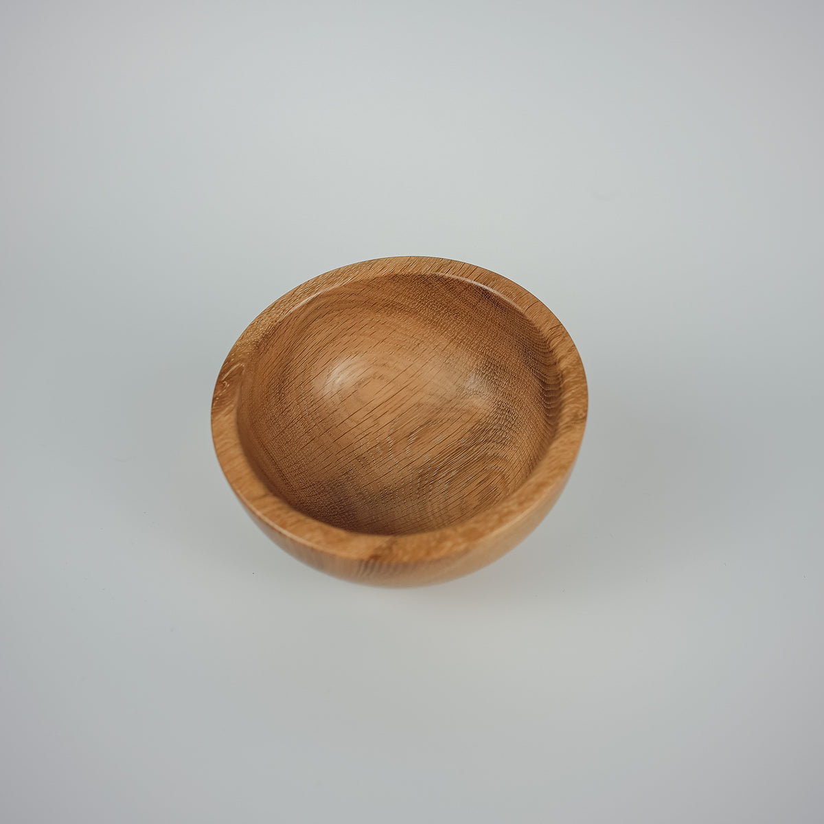 A small, round wooden bowl with a smooth, polished finish and visible wood grain, set against a plain light gray background.