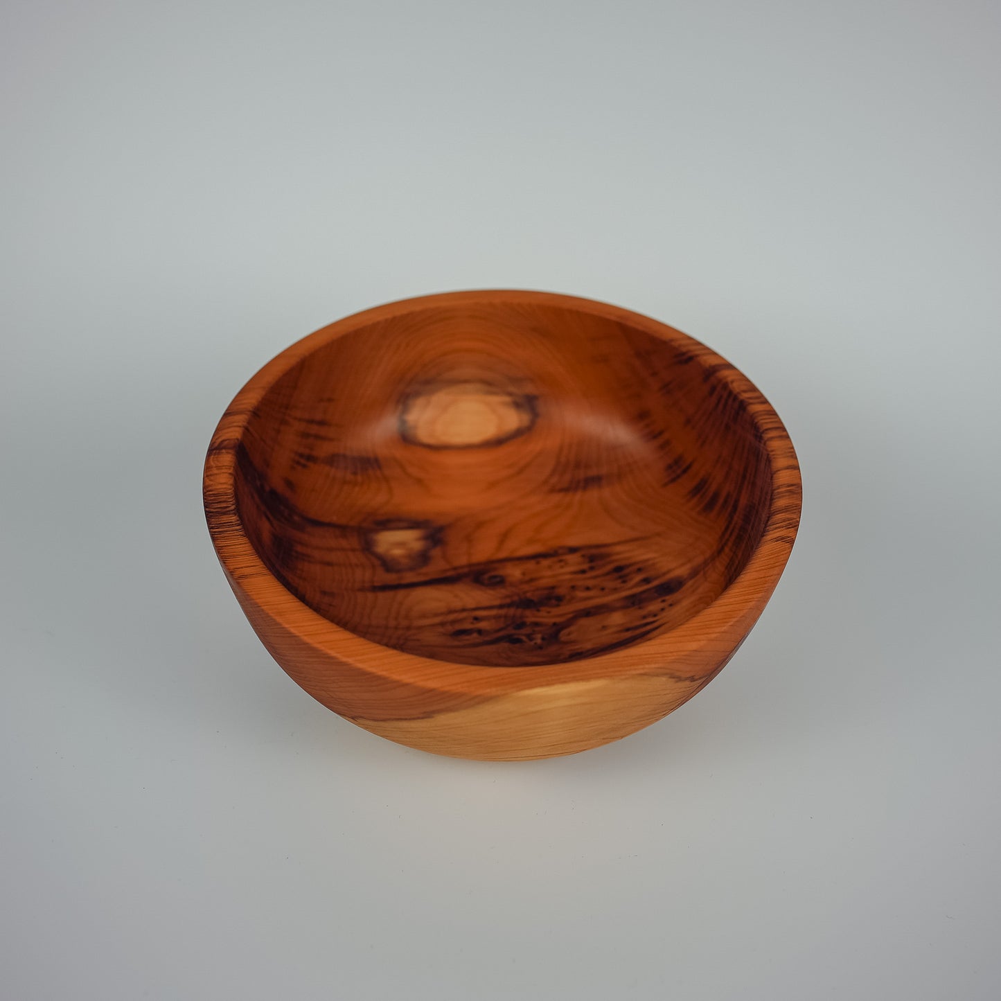 A handcrafted wooden bowl with a rich reddish-brown finish and prominent natural wood grain patterns, photographed on a neutral light gray background.
