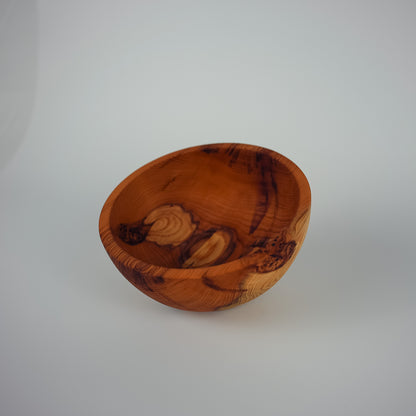 A handcrafted wooden bowl with a rich, swirling grain pattern in warm brown and orange tones, photographed on a neutral light gray background.