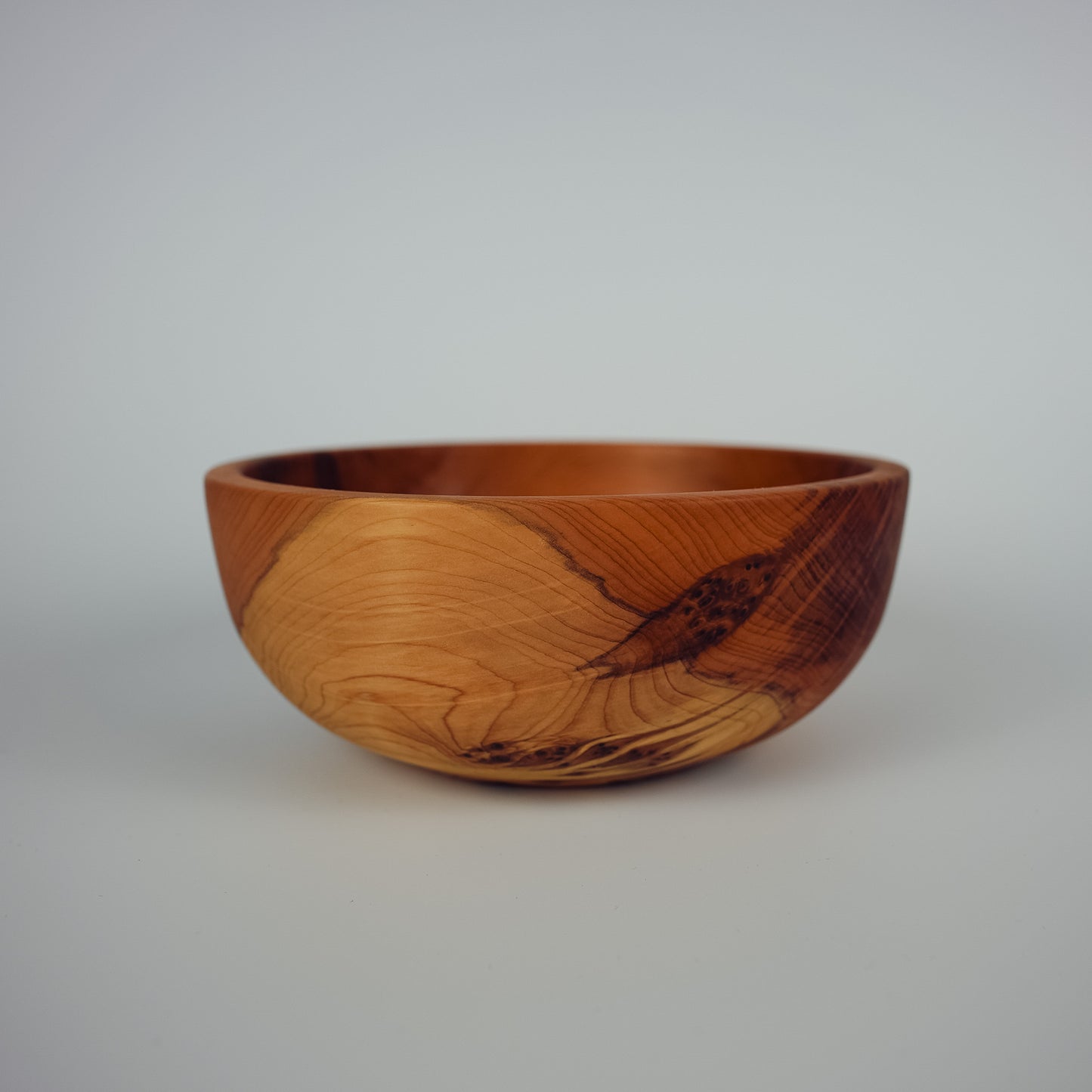 A handcrafted wooden bowl with a rich warm brown color and distinctive dark grain patterns, photographed against a neutral light gray background.