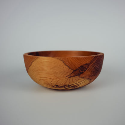 A handcrafted wooden bowl with a rich warm brown color and distinctive dark grain patterns, photographed against a neutral light gray background.