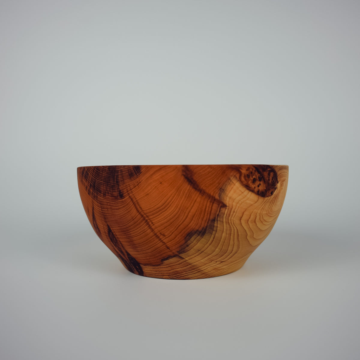 A handcrafted wooden bowl with a rich, swirling grain pattern in warm brown and golden tones, photographed against a neutral light gray background.