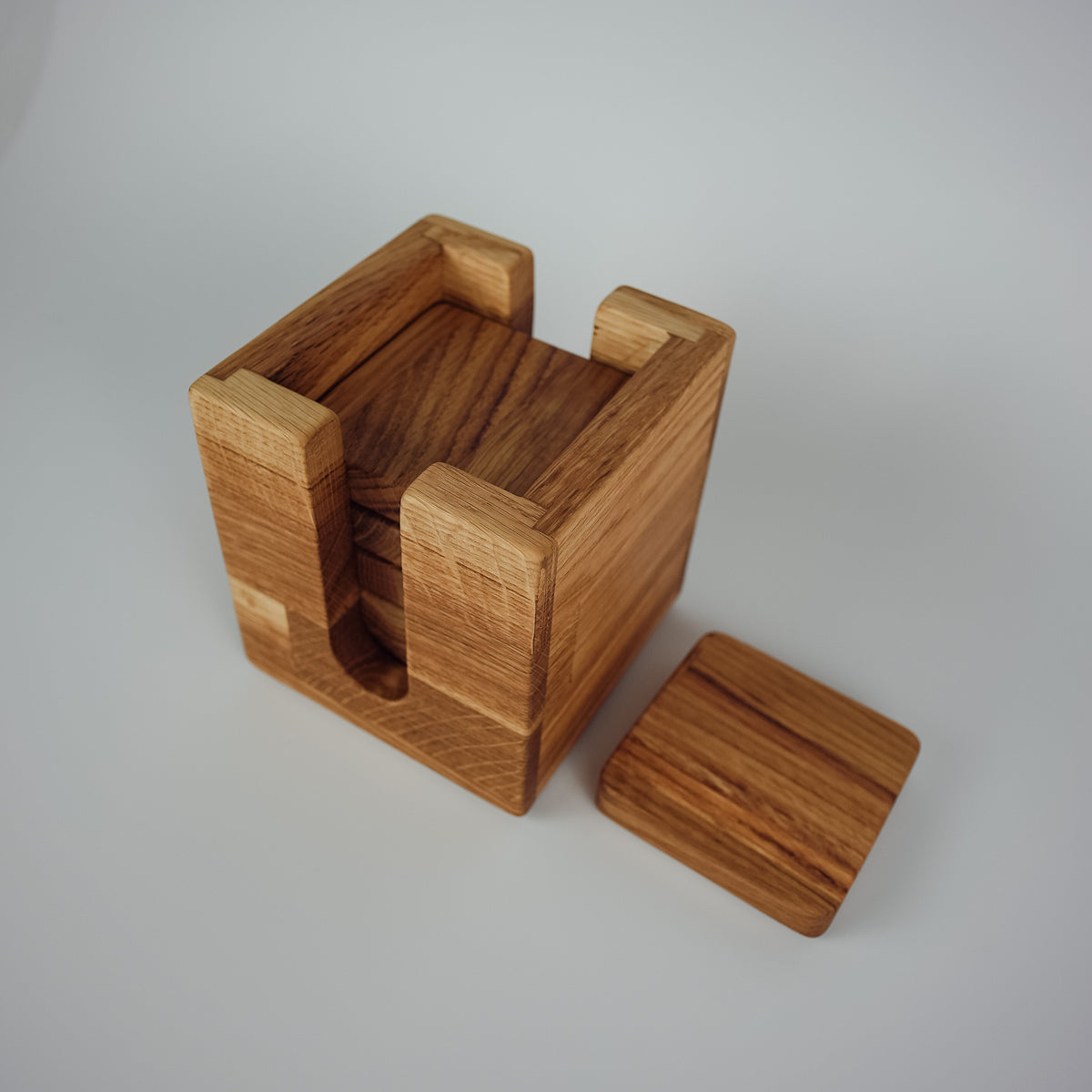 A square wooden box with a recessed center and a separate matching wooden lid placed beside it, photographed on a clean light gray studio background.