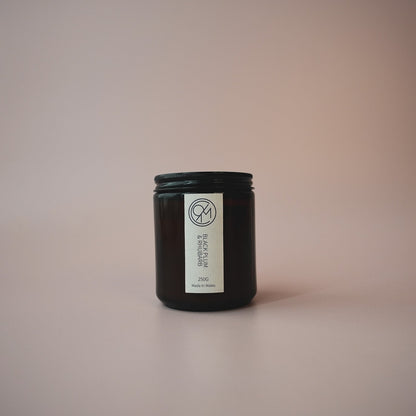 A small amber jar candle with a white label reading 'black plum & rhubarb' on a soft beige background.