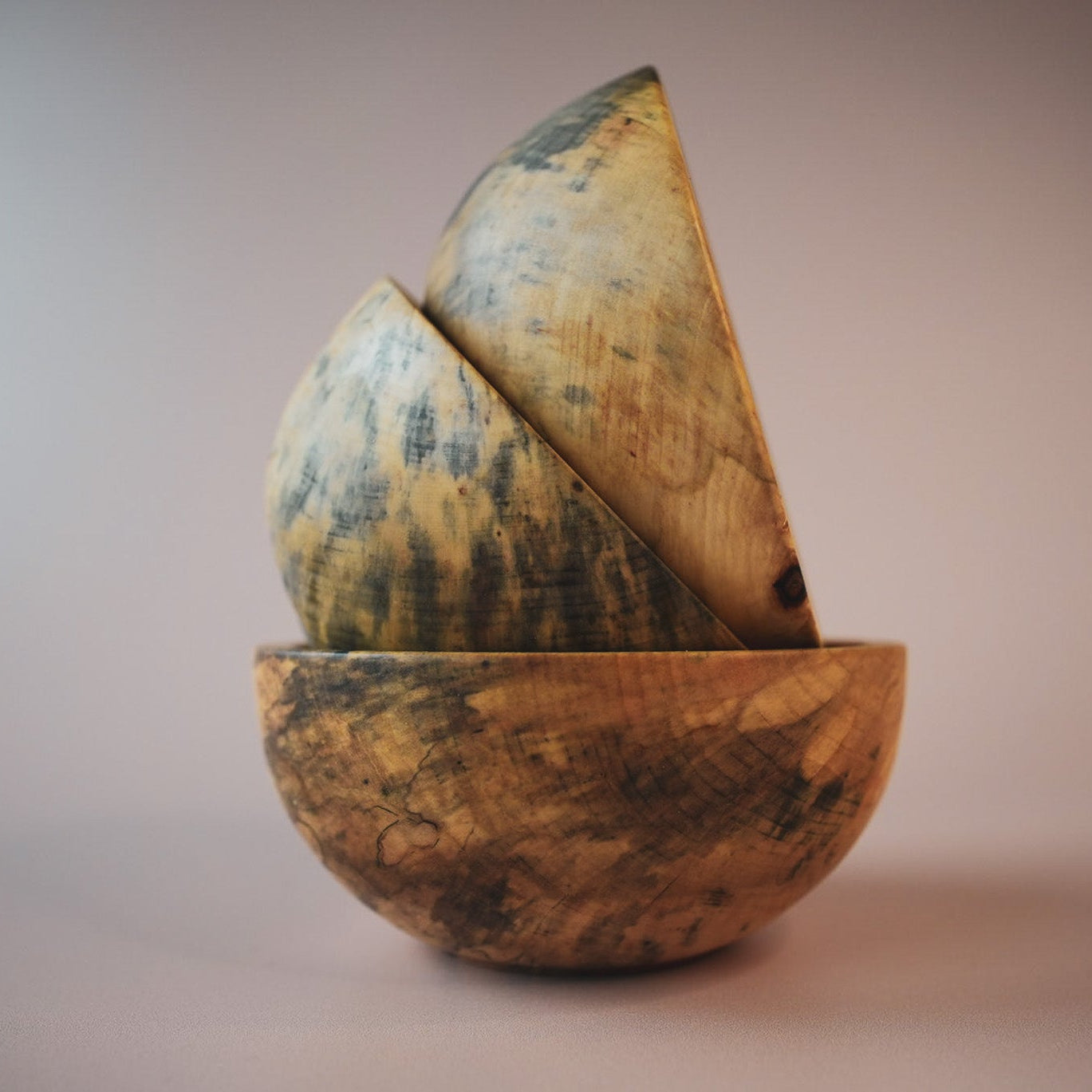 three wooden bowls stacked on top of one and other on a pink photography background